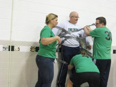 Photo of teachers using duct tape to tape the principal to the wall