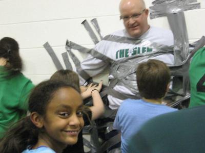 Photo of teachers and students using duct tape to tape the principal to the wall