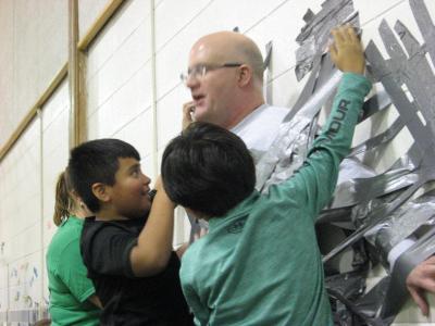 Photo of teachers and students using duct tape to tape the principal to the wall