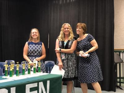 photo of three ladies standing next to a table of trophies