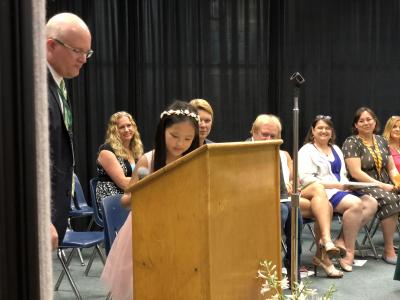 photo of student at podium on stage with adult supporting her