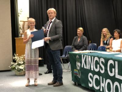 photo of student being congratulated by adult on a stage next to table with banner that reads kings glen school