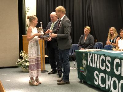 photo of student being congratulated by adult on a stage next to table with banner that reads kings glen school