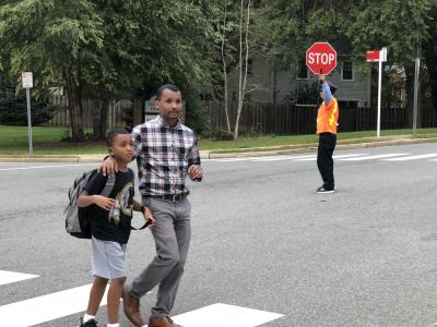 photo of student and parent walking thru crosswalk with crosswalk person holding stop sign