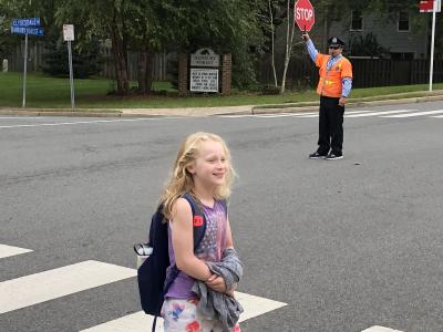 photo of studentwalking thru crosswalk with crosswalk person holding stop sign