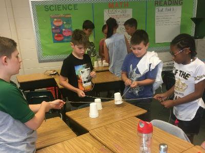 photo of students standing as a team with plastic cups and strings stacking cups