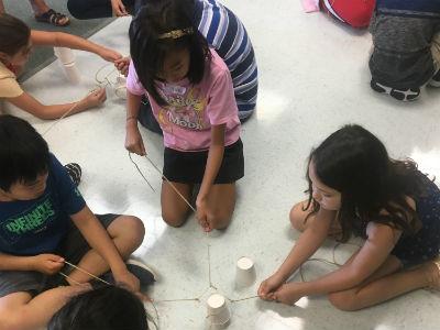 photo of students on floor with plastic cups and strings stacking cups